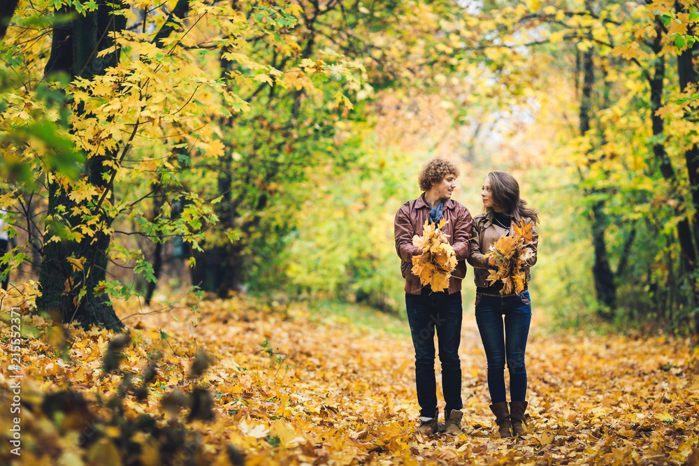 Loving happy couple in autumn in park holding autumn maple leaves in hands.