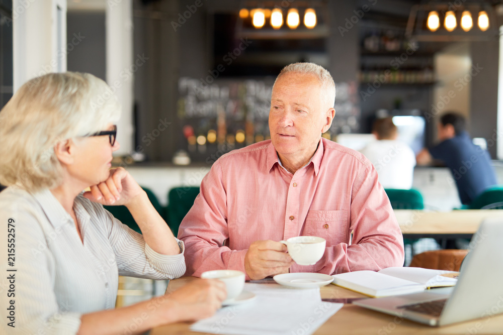 Two senior economists having tea-break in cafe and discussing some working points or ideas Two senior economists having tea-break in cafe and discussing some working points or ideas