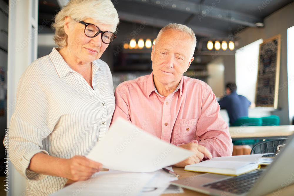 Senior man and woman reading one of financial documents during meeting in cafe Senior man and woman reading one of financial documents during meeting in cafe