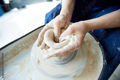 Hands of pottery master forming neck of jug during rotation of pottery-wheel