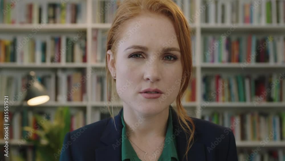 portrait of beautiful young red head business woman intern looking serious pensive at camera in library bookshelf background portrait of beautiful young red head business woman intern looking serious pensive at camera in library bookshelf background