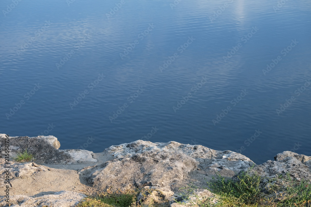 Calm Water View from the Rocky Shore Reflecting Clouds and Blue Sky Calm Water View from the Rocky Shore Reflecting Clouds and Blue Sky