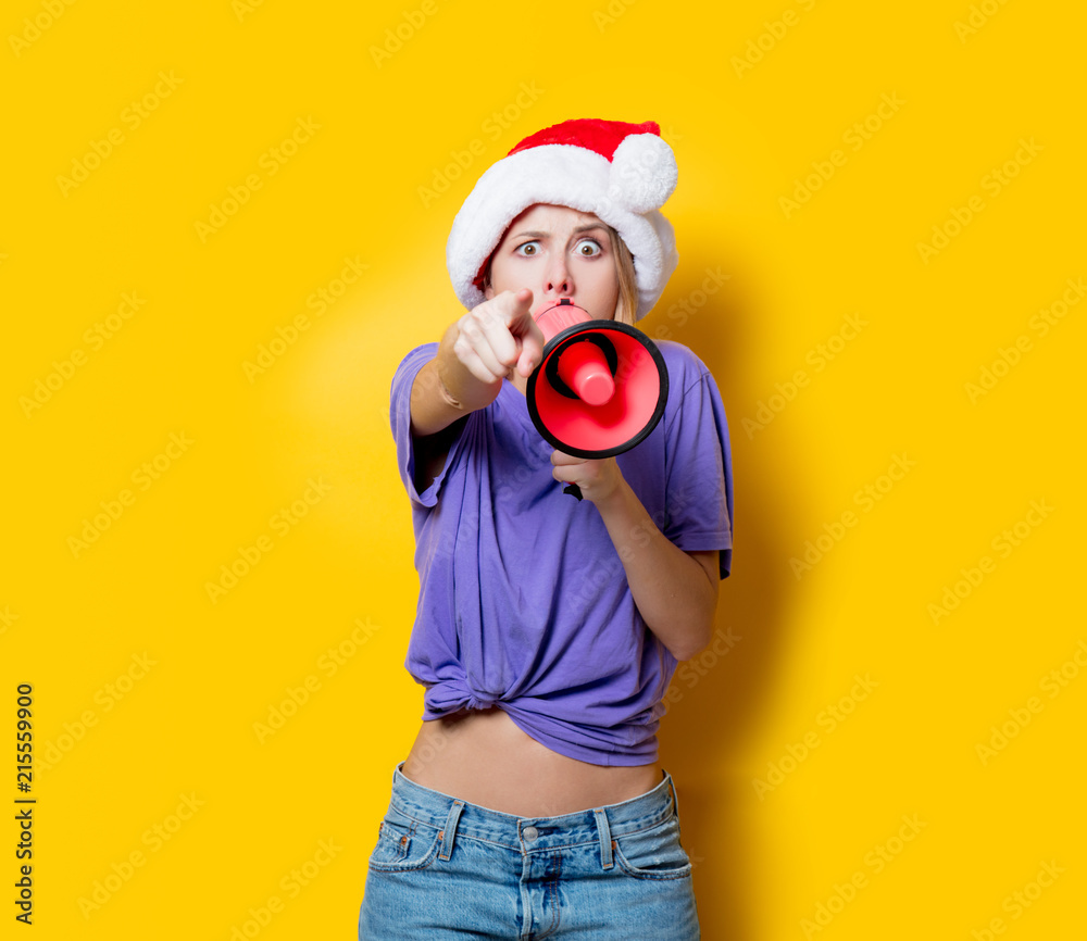 Fototapeta premium Young style girl in purple clothes and Christmas hat with pink megaphone on yellow background. Symbolizes female resistance. Clothes in 1980s style