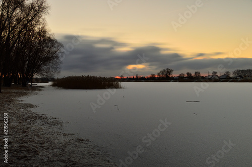 Brzeg zamarzniętego jeziora oświetlony wschodzącym słońcem w zimie. © W Korczewski