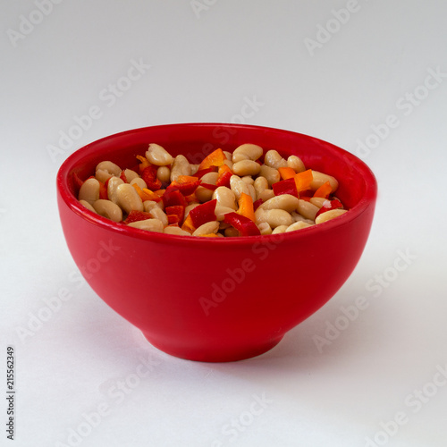 Navy beans and red and orange peppers in red bowl isolated on white