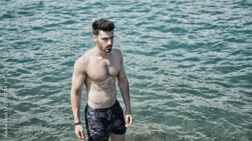 Handsome muscular young man standing on a beach, relaxed, shirtless