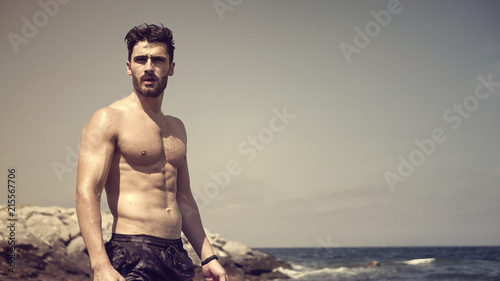 фотографія Handsome muscular young man standing on a beach, relaxed, shirtless