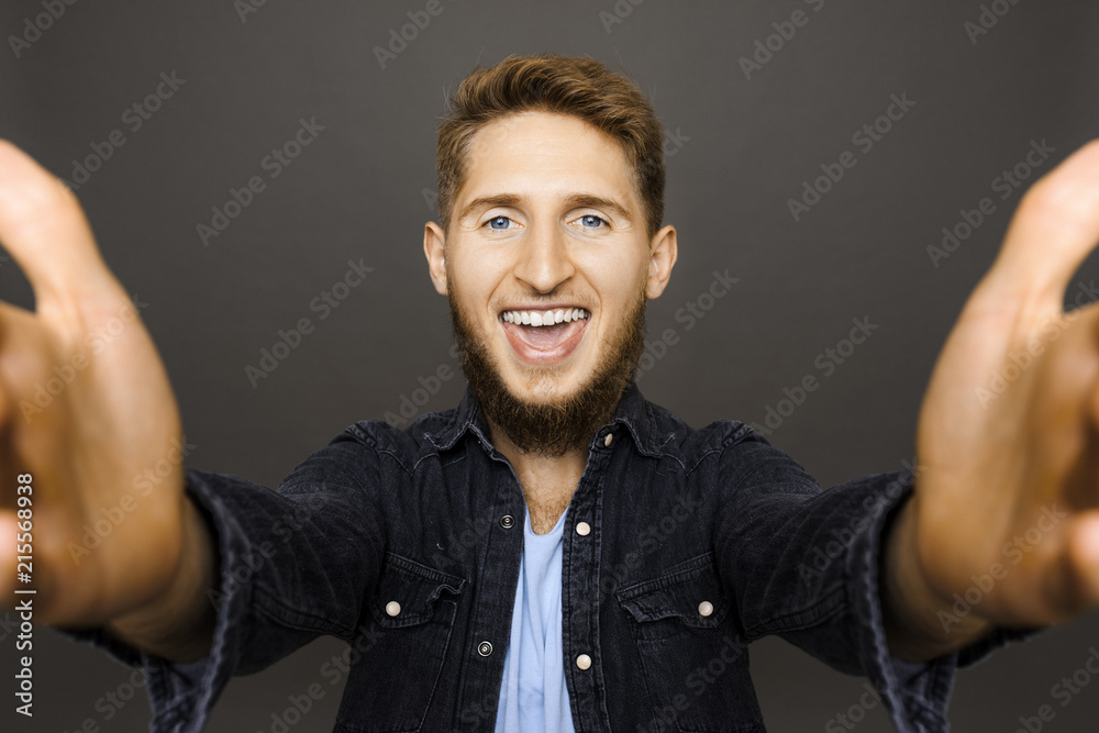 Casual bearded man in denim outstretching hands toward camera looking super excited on gray background Casual bearded man in denim outstretching hands toward camera looking super excited on gray background