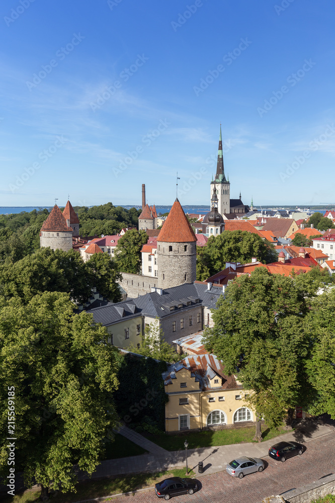 City walls' and St. Olaf's (or Olav's) church's towers and other buildings at the Old Town in Tallinn, Estonia, viewed from above on a sunny day in the summer.