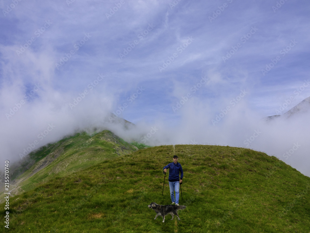 An active elderly man does walks in the mountains with his dog.