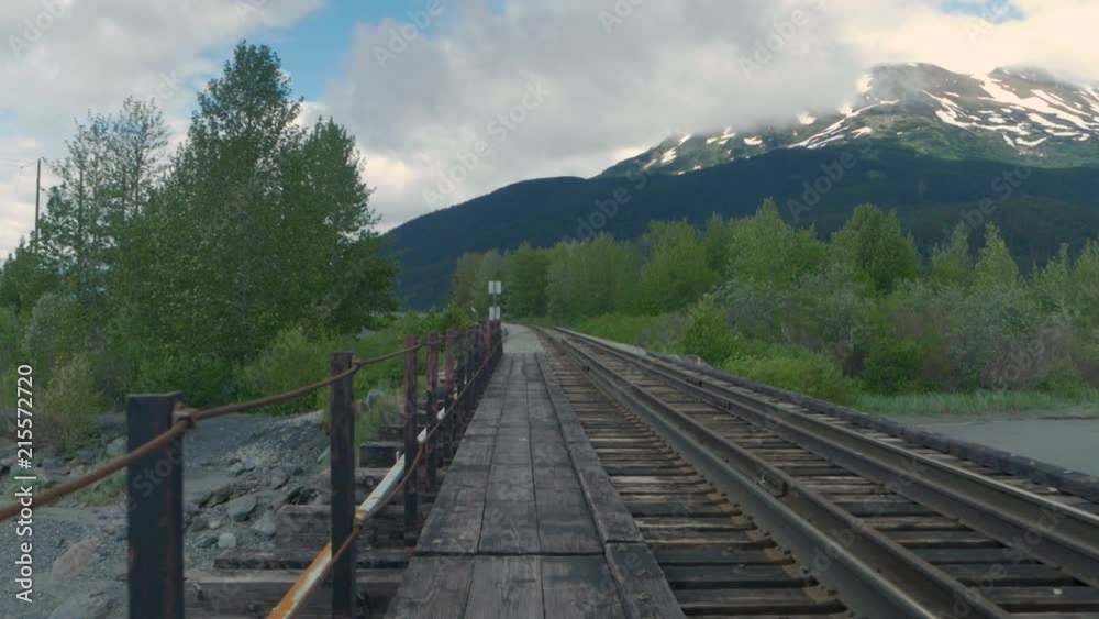 Slow motion walk along a railroad bridge in Alaska, with snow-capped mountains, and lush green forest in the background. Slow motion walk along a railroad bridge in Alaska, with snow-capped mountains, and lush green forest in the background.