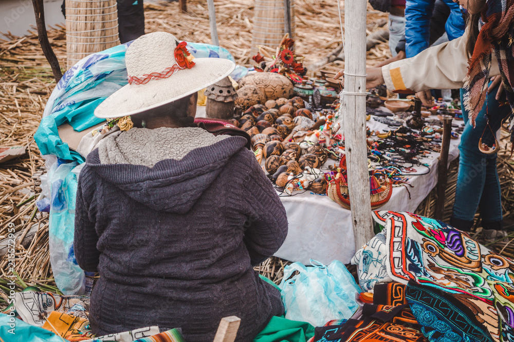 Young Peruvian woman in a large straw hat sells her handmade jewelry, cloth and other trinkets to western tourists on Los Uros floating islands in Puno,  Peru