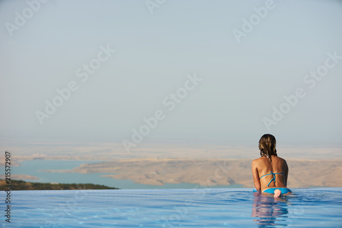 Young woman relaxaing in the swimming pool looking at the nature landscape view on background. Travel, summer holiday concept