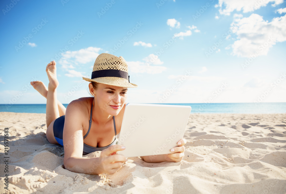 young woman in swimwear on beach using tablet PC