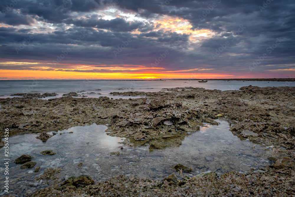 Sunrise over cotal reefs at low tide in Australia. The sun is rising in the background. 