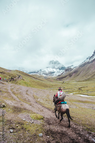 Traditional indigenous Quechua horseman rides his horse across the valleys of the Cusco region of Peru, next to Rainbow Mountain (or Montaña de Siete Colores)