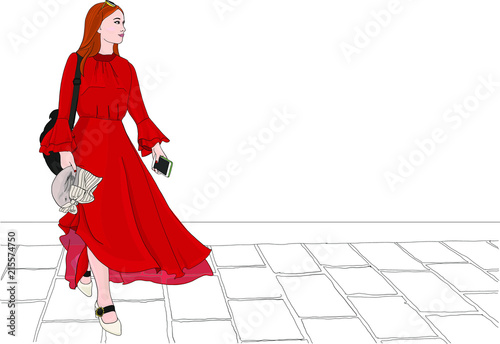 Stylish, fashionable woman in a flowing red dress with transparent chiffon walks over a cobblestone street  in a European city.