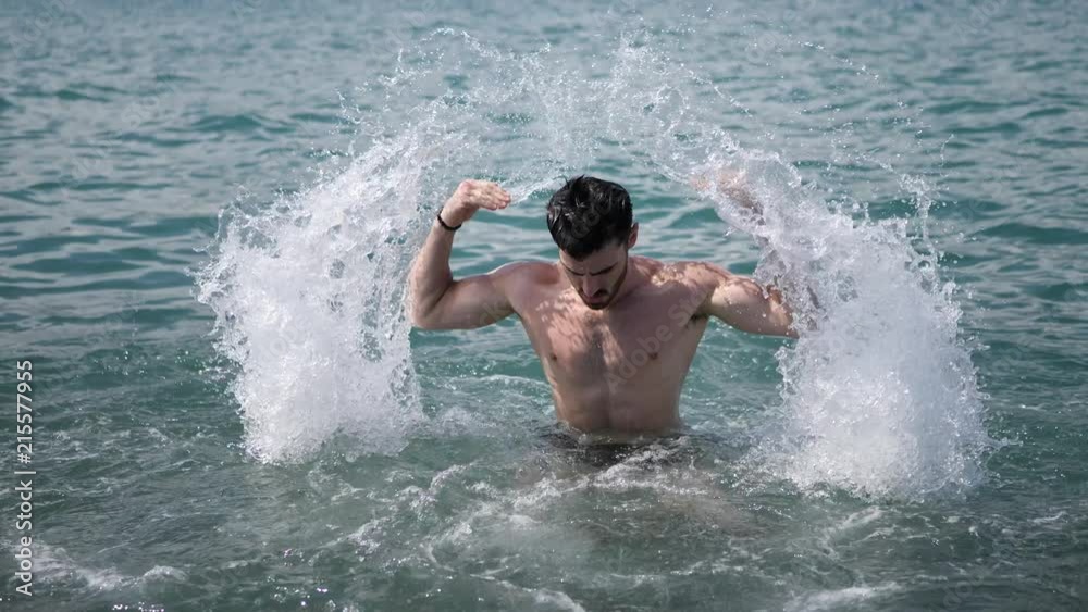 Handsome, hot young muscular man in the sea, splashing water up, showing his muscular torso and arms Handsome, hot young muscular man in the sea, splashing water up, showing his muscular torso and arms