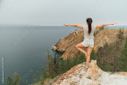 girl doing yoga on a rock near lake Baikal. Summer yoga practice in nature. Alone.