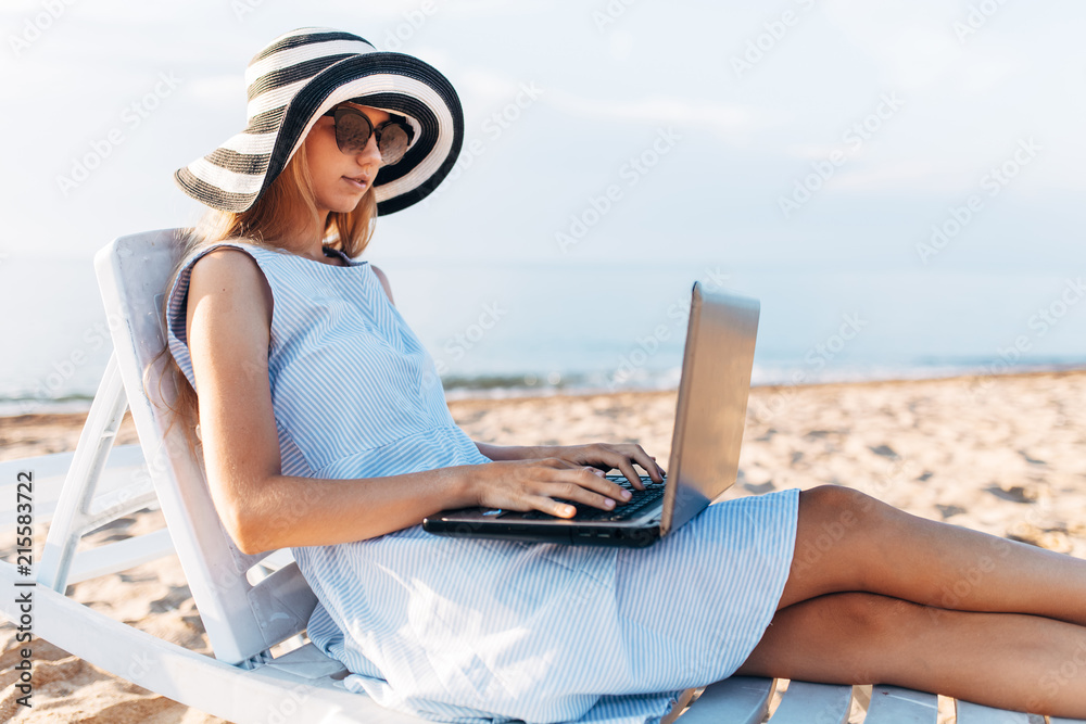 Freelancer girl working on vacation, in front of the beautiful sea, sitting with a laptop on the ocean