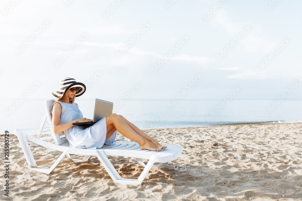 Freelancer girl working on vacation, in front of the beautiful sea, sitting with a laptop on the ocean