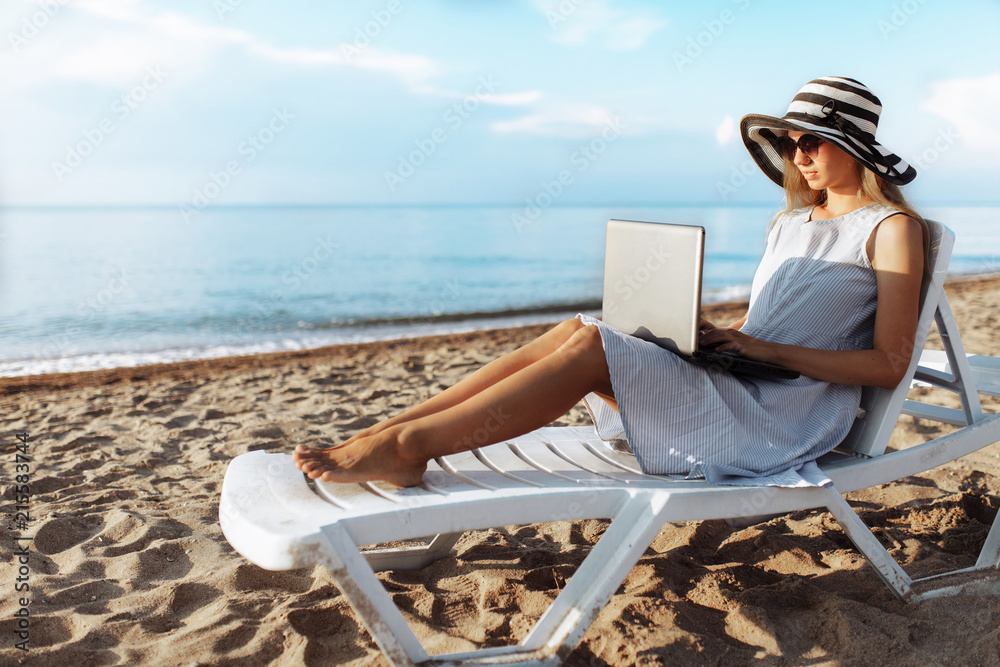 Beautiful girl sitting with a laptop on a chaise longue, a woman working on vacation, job search