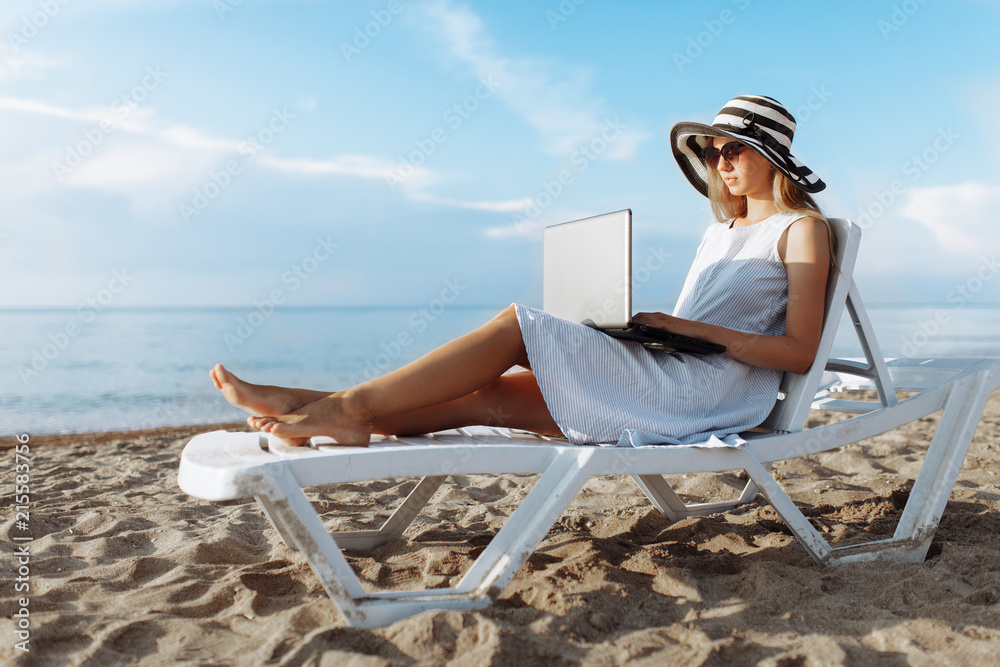 Beautiful girl sitting with a laptop on a chaise longue, a woman working on vacation, job search