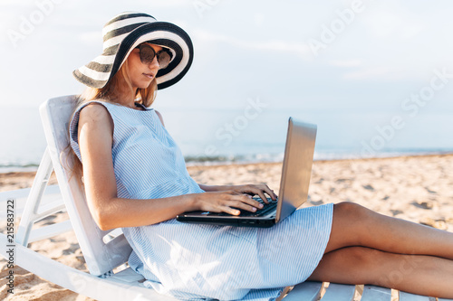 Freelancer girl working on vacation, in front of the beautiful sea, sitting with a laptop on the ocean © Shopping King Louie