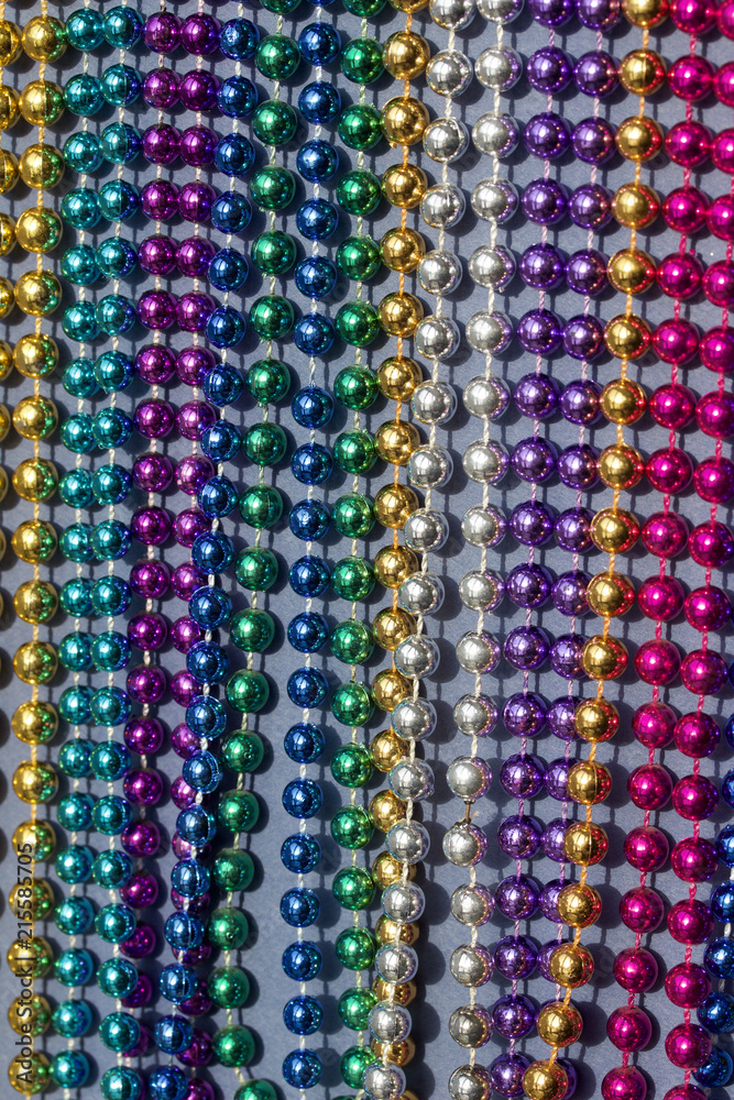 Multi-color Mardi Gras beads in rows on neutral blue background