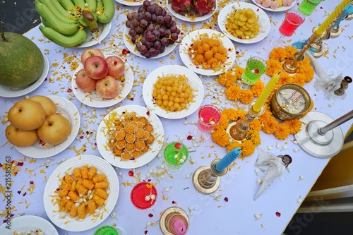 Top view of holy worship with Thai dessert, colorful water, fruit, flowers and candle to worship on the table, Religion concept