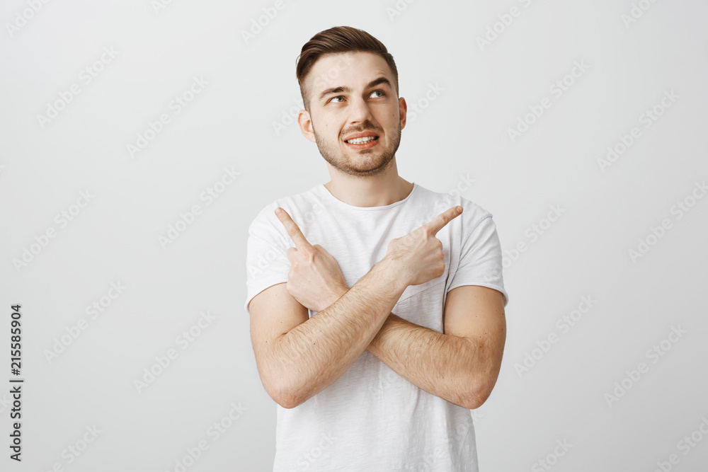 Unsure worried guy feeling nervous making wrong decision standing intense over gray background in white t-shirt crossing hands on chest pointing left and right being in doubts and hesitating Unsure worried guy feeling nervous making wrong decision standing intense over gray background in white t-shirt crossing hands on chest pointing left and right being in doubts and hesitating