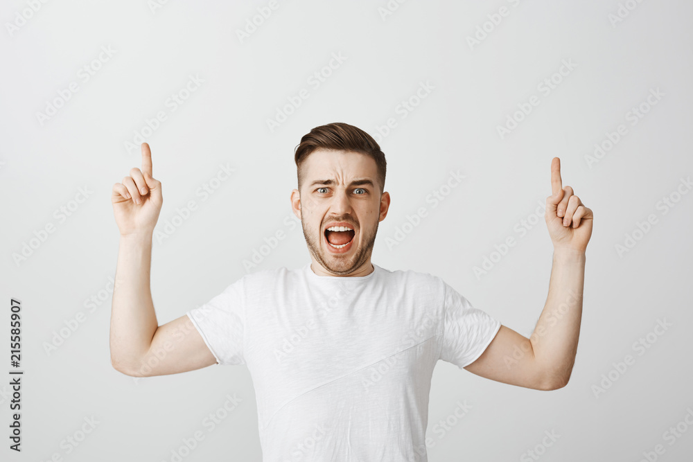 Pissed and angry dissatisfied good-looking mature male customer in white t-shirt raising hands pointing up and yelling feeling intense and irritated demanding refund shouting in anger over gray wall Pissed and angry dissatisfied good-looking mature male customer in white t-shirt raising hands pointing up and yelling feeling intense and irritated demanding refund shouting in anger over gray wall