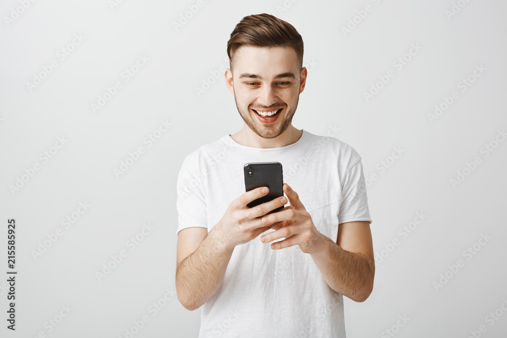 Portrait of impressed good-looking bearded guy with stylish brown hairstyle holdign smartphone and gazing thrilled and amused at smartphone screen using cool app cannot stop playing in device Portrait of impressed good-looking bearded guy with stylish brown hairstyle holdign smartphone and gazing thrilled and amused at smartphone screen using cool app cannot stop playing in device