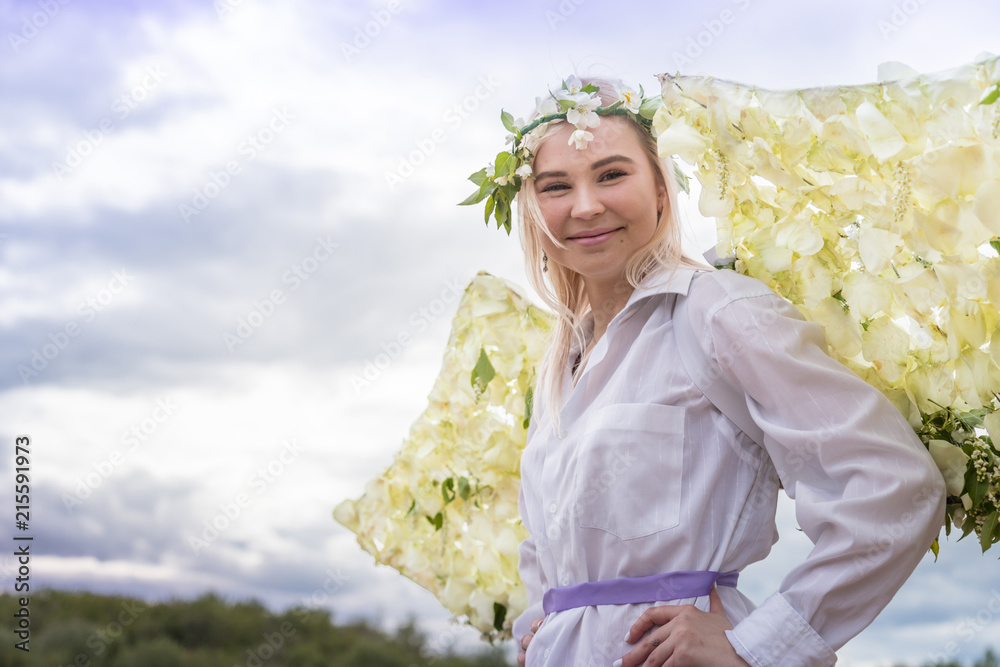 Nice blonde girl with white flower wings and cloudy sky background