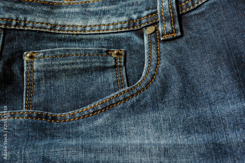 Close-up of a piece of blue jeans with orange stitches. Pocket with rivets close-up. Close-up of a piece of blue jeans with orange stitches. Pocket with rivets close-up.