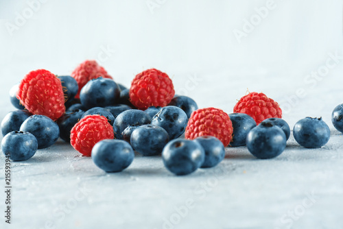 Blueberries and raspberries on the background of gray cement. Ripe and juicy fresh raspberries and blueberries close-up. A lot of berries close-up.