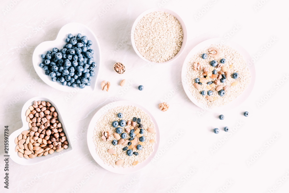 Ingredients for cooking healthy breakfast. Blueberries, nuts, oat flakes, dried fruits,raisins on a light marble table. Healthy food concept. Flat lay, top view, copy space 