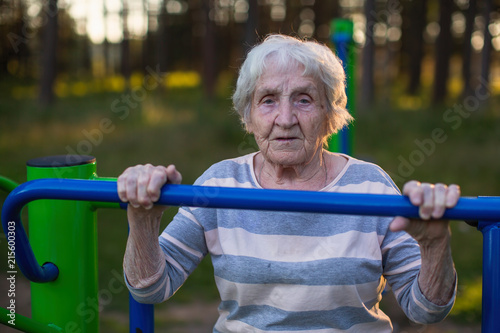 Very elderly woman doing morning exercise on the street sport playground.