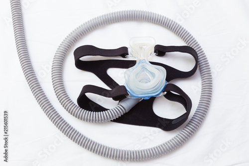 CPAP mask and hose with headgear on white bed