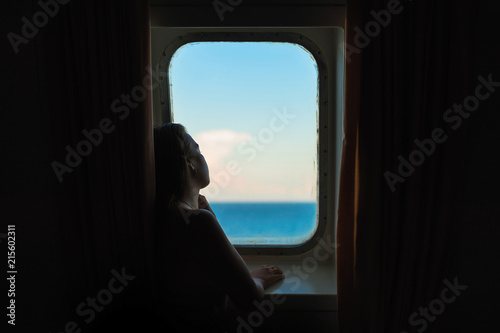 beautiful young naked female looking through the ship window on the Greek islands and the Ionian sea at sunset © flowertiare