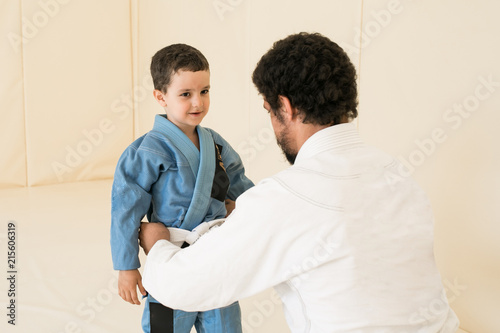 Male karate instructor training little child in dojo or jiu-jitsu at gym at tatami. Father and son are preparing for training. Sport and healthy family concept