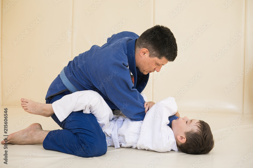 Male karate instructor training little child in dojo or jiu-jitsu at gym at tatami. Trainer teaches kid the basics of fighting for self-defense