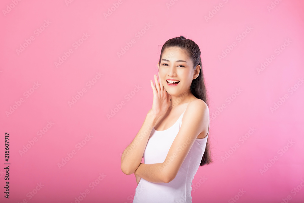 Portrait of a smiling attractive woman in white tanktop outfit posing while standing and smiling at camera isolated over pink background. Portrait of a smiling attractive woman in white tanktop outfit posing while standing and smiling at camera isolated over pink background.