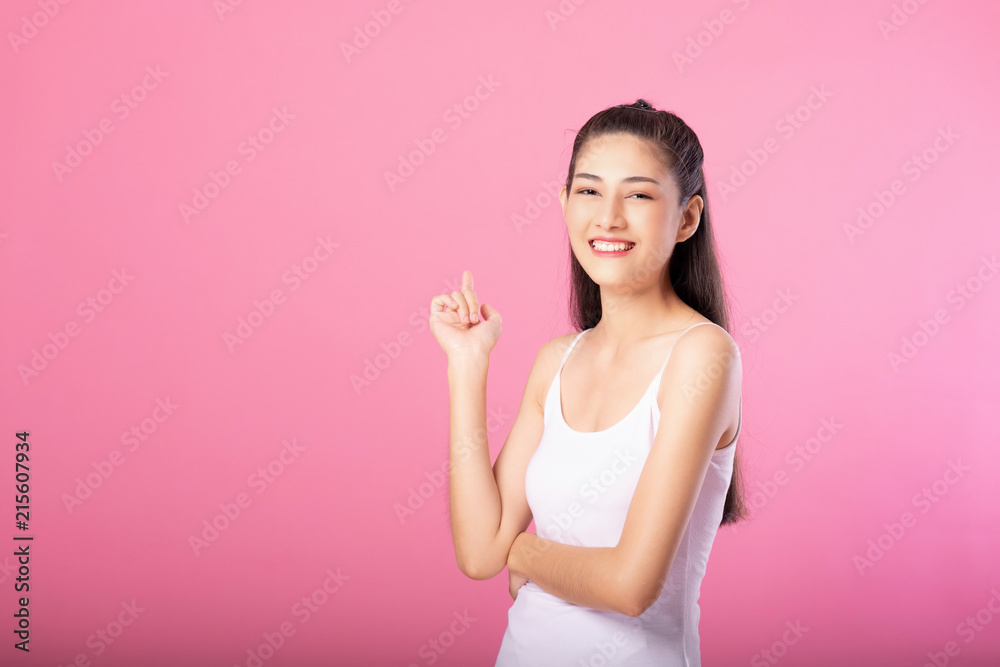 Portrait of a smiling attractive woman in white tanktop outfit posing while standing and smiling at camera isolated over pink background. Portrait of a smiling attractive woman in white tanktop outfit posing while standing and smiling at camera isolated over pink background.