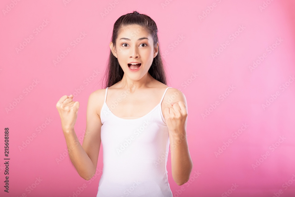 Portrait of a smiling attractive woman in white tanktop outfit with winning exciting pose while standing and smiling at camera isolated over pink background. Portrait of a smiling attractive woman in white tanktop outfit with winning exciting pose while standing and smiling at camera isolated over pink background.
