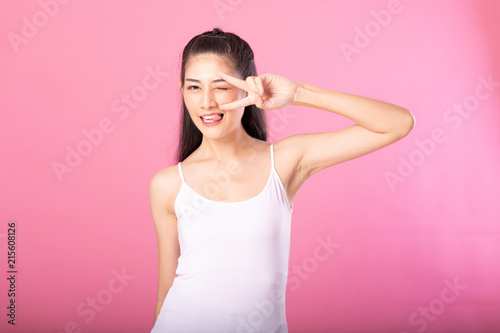 Portrait of a smiling attractive woman in white tanktop outfit with victory pose while standing and smiling at camera isolated over pink background.