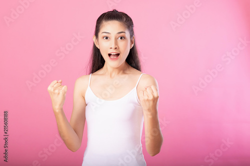 Portrait of a smiling attractive woman in white tanktop outfit with winning exciting pose while standing and smiling at camera isolated over pink background.
