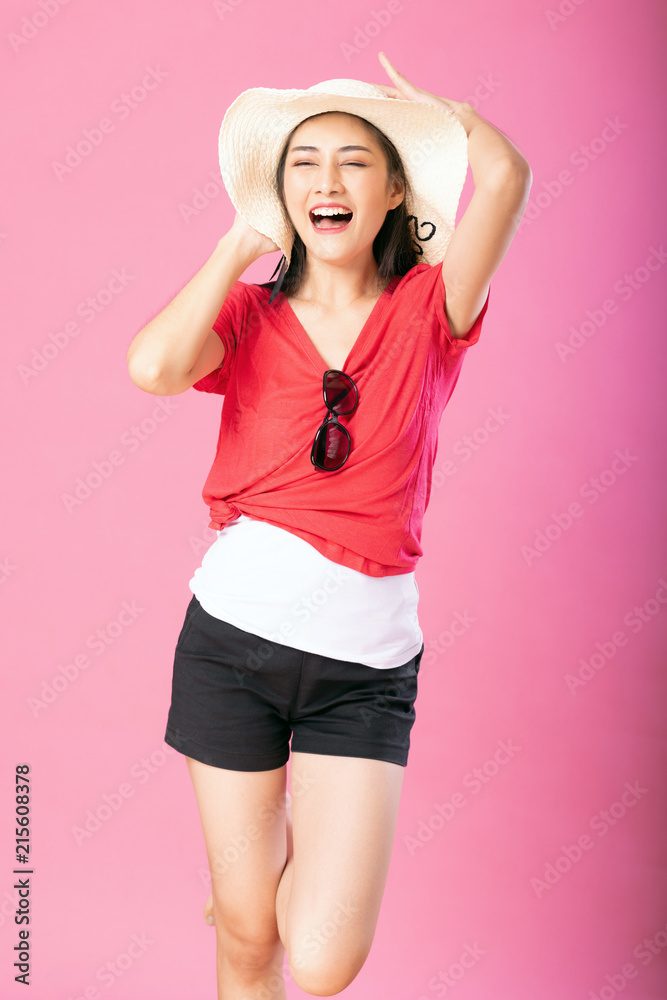 Portrait of a smiling attractive woman in summer outfit and hat posing while standing and looking at camera isolated over pink background. Portrait of a smiling attractive woman in summer outfit and hat posing while standing and looking at camera isolated over pink background.