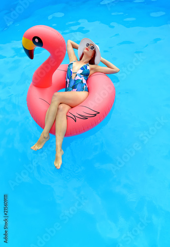 A young woman wearing a bathing suit and  a white summer hat sits relaxed in an  inflatable swim ring.  © Brigitte