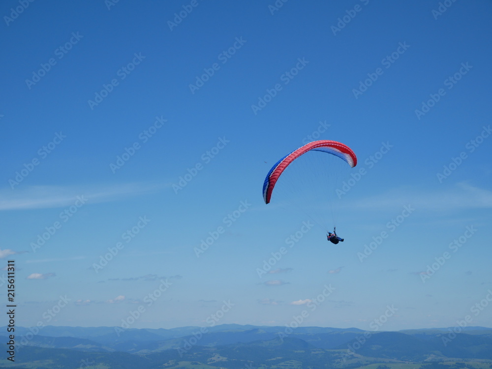Carpathians / Ukraine - July 07 2017: Paraglider flying parachute in blue sky at a bright sunny summer day. Active lifestyle Carpathians / Ukraine - July 07 2017: Paraglider flying parachute in blue sky at a bright sunny summer day. Active lifestyle